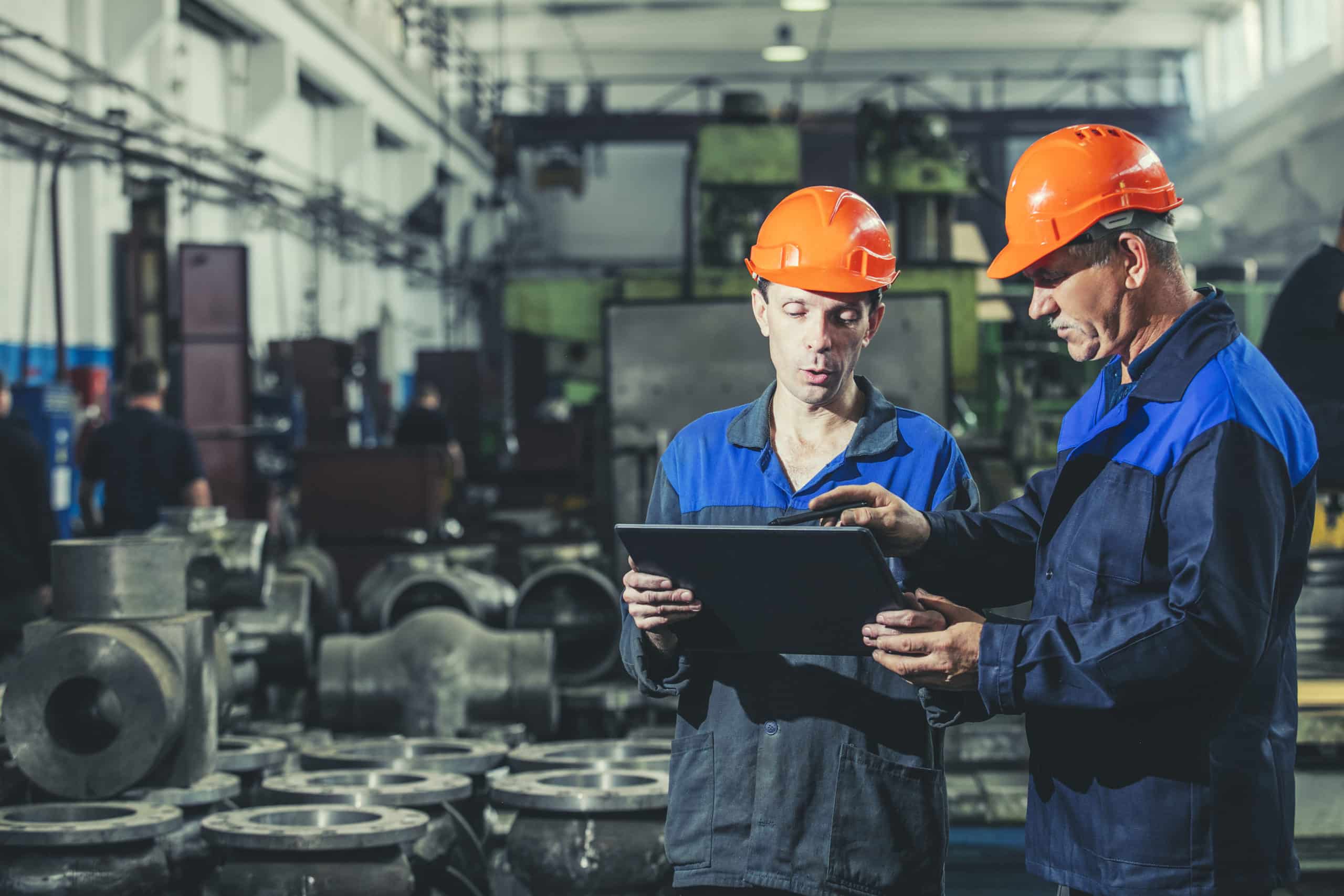 Two workers at an industrial plant with a tablet in hand, working