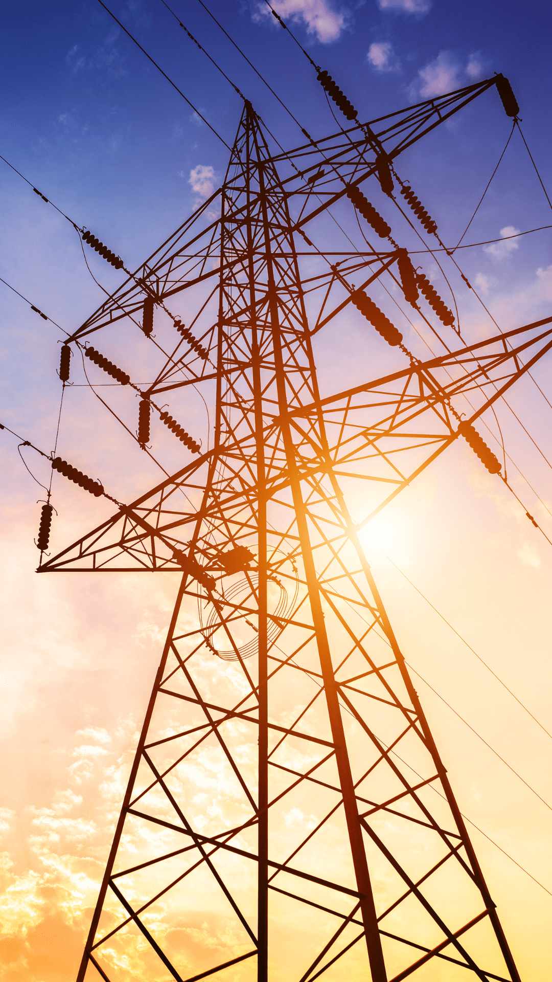 Utility worker with tablet at transmission pylon at dusk